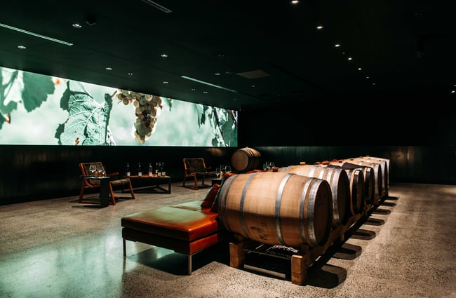 Wine bottles and plush seats sitting in a room with a large screen on the wall.