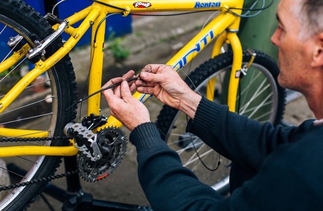Close up of a man working on a yellow bike with a blue logo.
