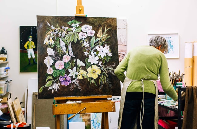 A woman painting flowers with a black background.