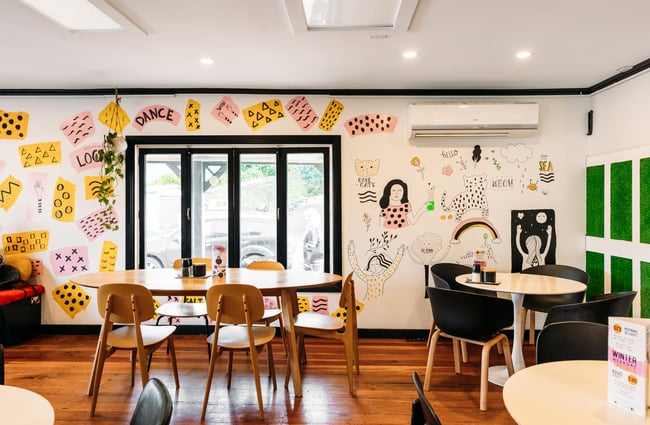 The seating area inside a cafe with white walls decorated in illustrations.
