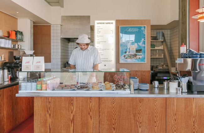 A staff member wearing a hat behind the counter of the Supreme cafe in Christchurch.