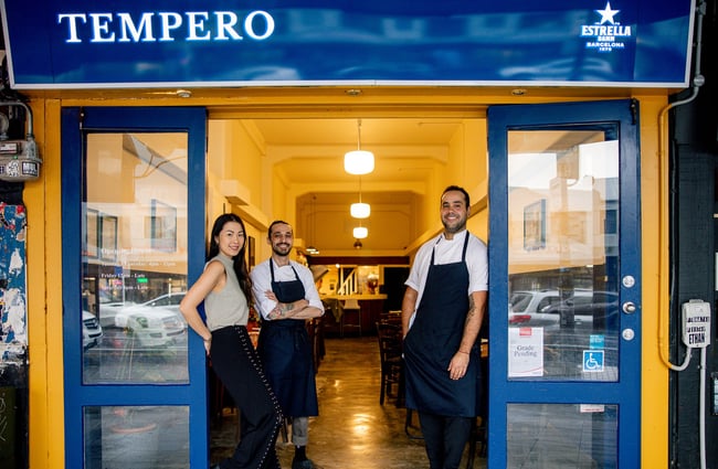 Two men and a woman standing in the bright blue entrance to Tempero restaurant in Auckland.