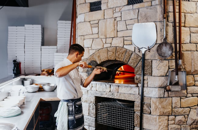 A chef putting a pizza into a wood fired oven.