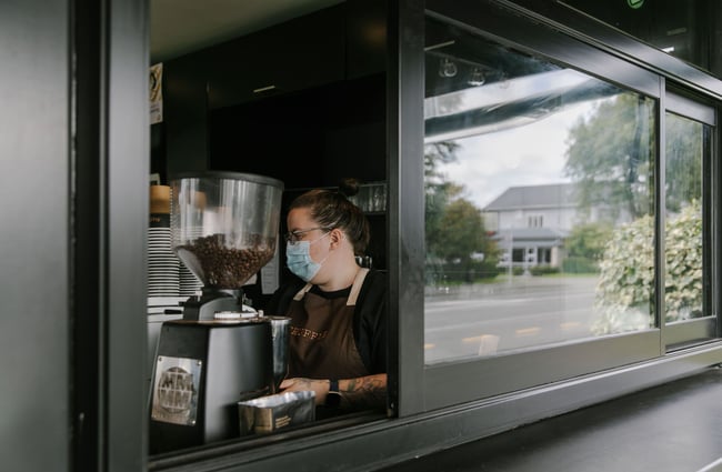Person making a coffee looking through a small hatch window at Truffle café, Christchurch.