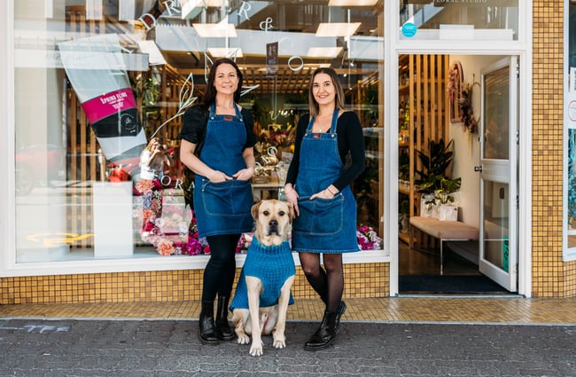 Two women and a dog standing outside their shop.