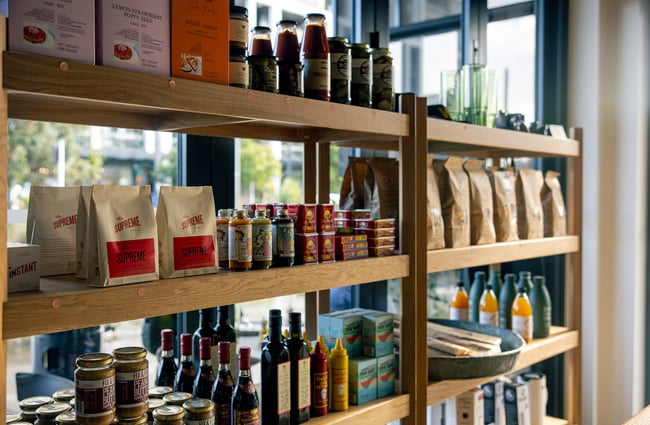 A close up of pantry goods and bags of coffee on display on wooden shelves.