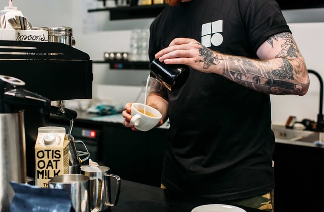 Milk being poured into a white coffee cup by a barista.