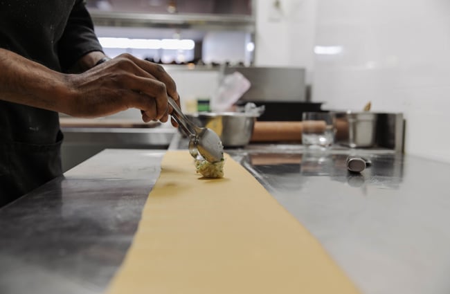 Chef spooning filling onto sheet of pasta to make ravoli.
