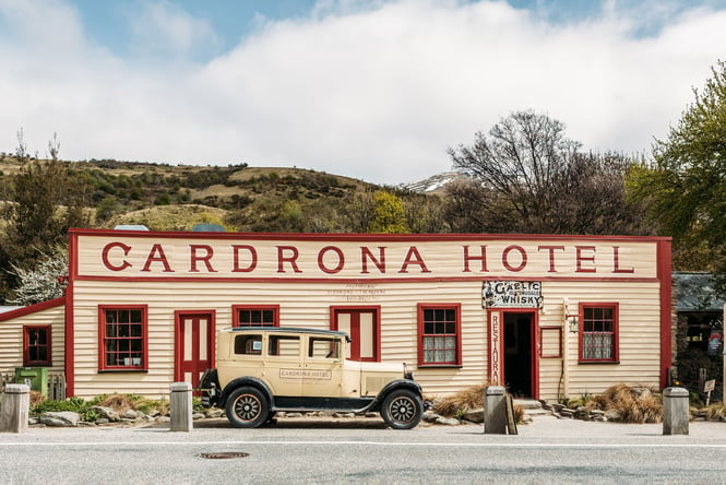 Historic cream and maroon weatherboard frontage of Cardrona Hotel with a vintage cream 1968 Chrysler Model 62 parked in front.