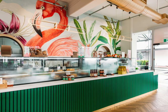The green counter inside Long Island Delicatessen with a backdrop of a flamingo painted on the wall.