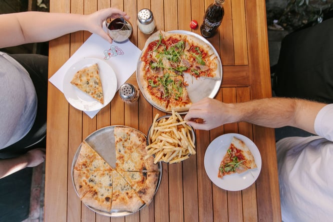 Birds eye view of two pizza and fries on wooden outdoor table.