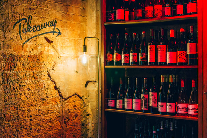 Shelves of wine with a takeaway sign.