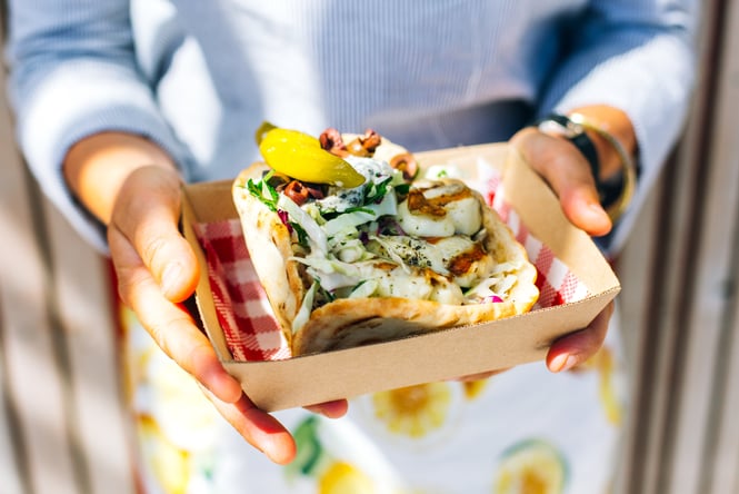 A souvlaki in a cardboard container in the hands of a customer.