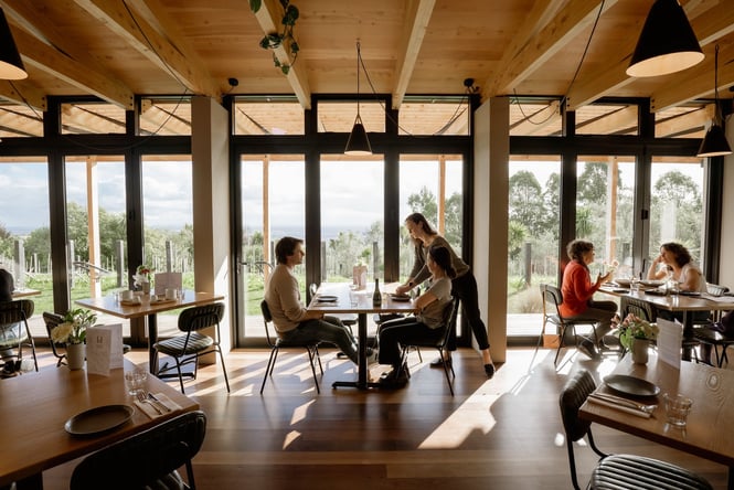 Interior of Tussock Hill restaurant with customers dining against the panoramic windows that look out over the Christchurch Port Hills.