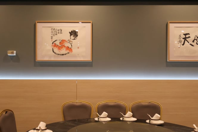 An orange, black and white art work in a gold frame on the wall above a table.
