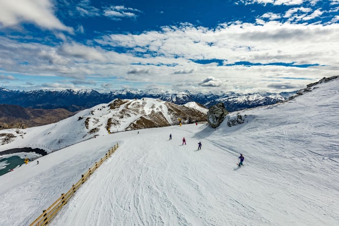 People skiing on Coronet Peak ski fields on sunny day.