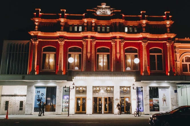 The Isaac Theatre Royal lit up at night time with bright orange lights.