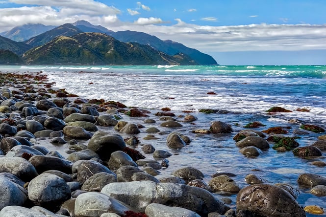 A view of a rocky beach on a sunny day with the mountains in the background.