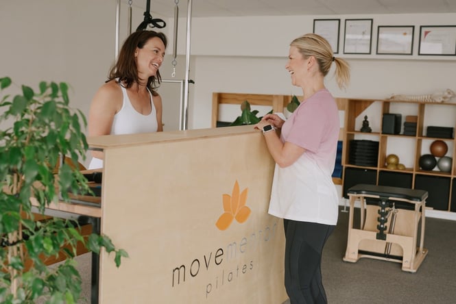 A student and staff member smiling at each other over a counter at Movementor Pilates.