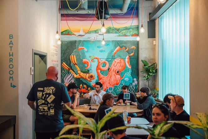 A photo of people sitting inside a restaurant with a painted octopus on the wall.