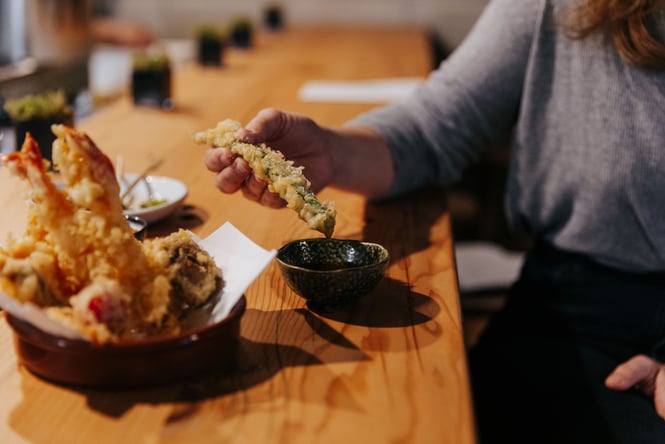 A hand holding a tempura asparagus at the bar at Bar Yoku.