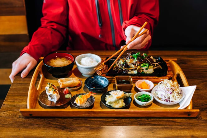 Small plates of Japanese food on a table in front of a person holding a pair of chopsticks.