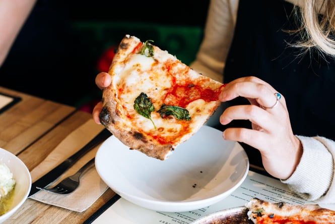A close up of hands holding a slice of margherita pizza.