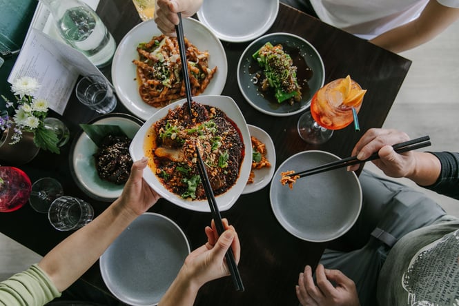 A flatlay of plates of food on a table and people helping themselves.