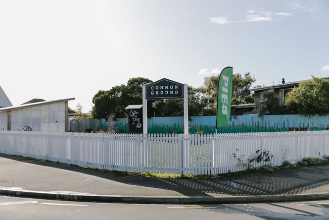 A white picket fence and Common Ground sign on grass.