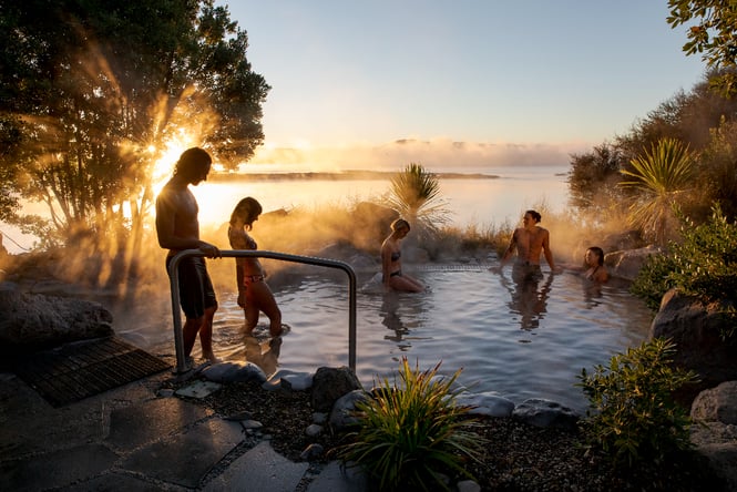 A group of people hopping into an outdoor spa with the sun setting behind them.