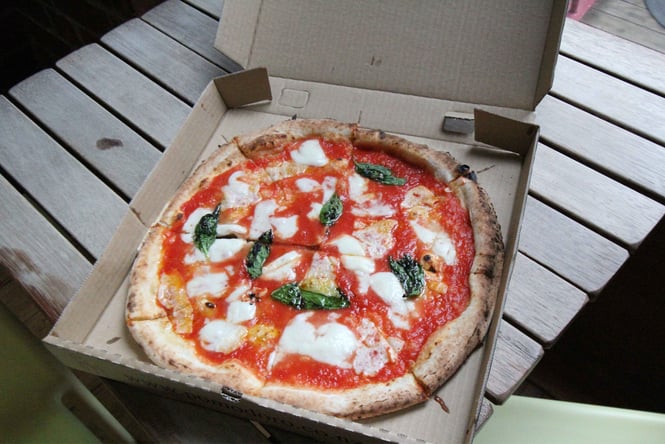 Margarita pizza in a box on a picnic table.