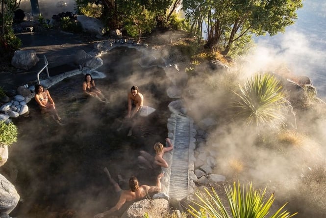 5 people sitting in a steaming hot pool surrounded by rocks and bushes.