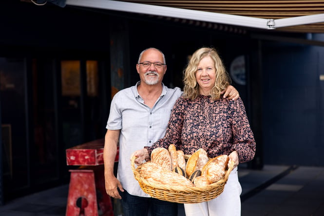 A man and woman holding a basket of bread smiling to camera.