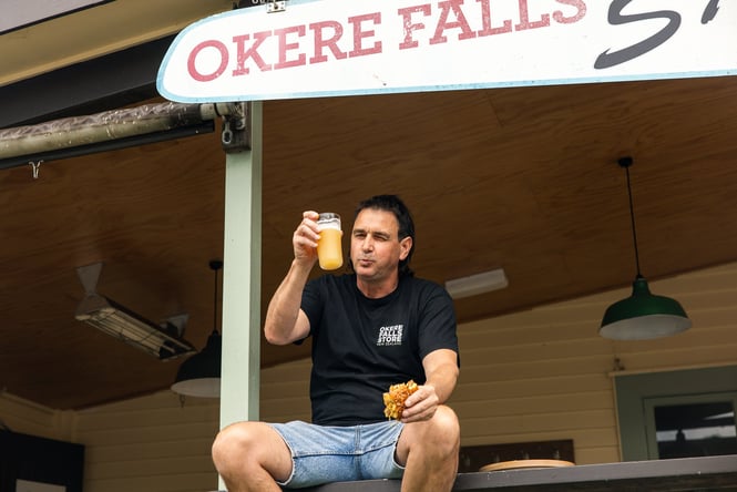 A man sitting on a porch eating a burger and drinking a pint of beer.