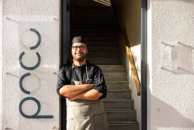A chef standing next to a sign next to the entrance of a building.