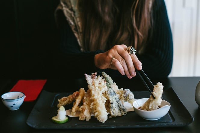 A close up of a woman's hand dipping tempura into a bowl of soy sauce.