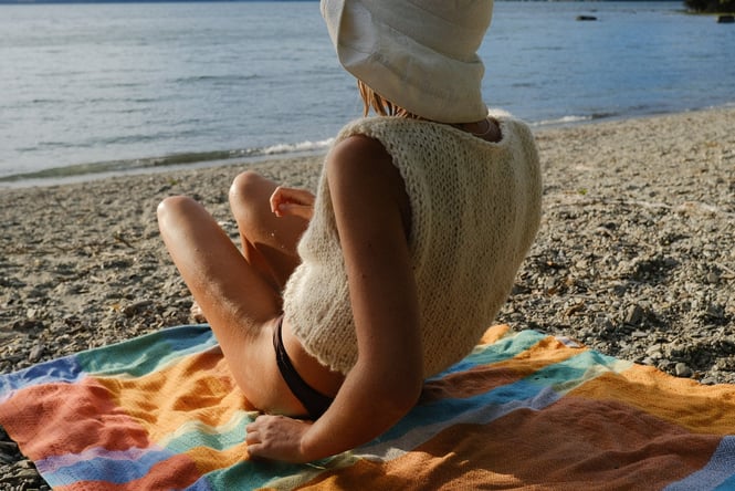 A woman sitting at the beach on a sunny day with her back to the camera.