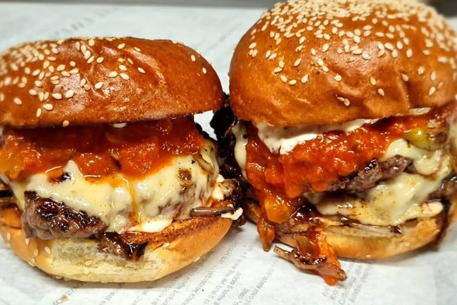 Two burgers with melted cheese over the burger patty.