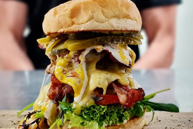 A very tall burger with lettuce, tomatoes, bacon, Patty, pickles and melted cheese.