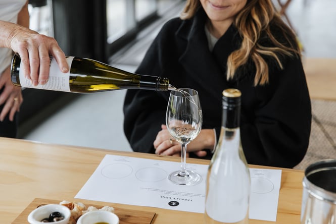 White wine being poured into a glass in front of a woman sitting.