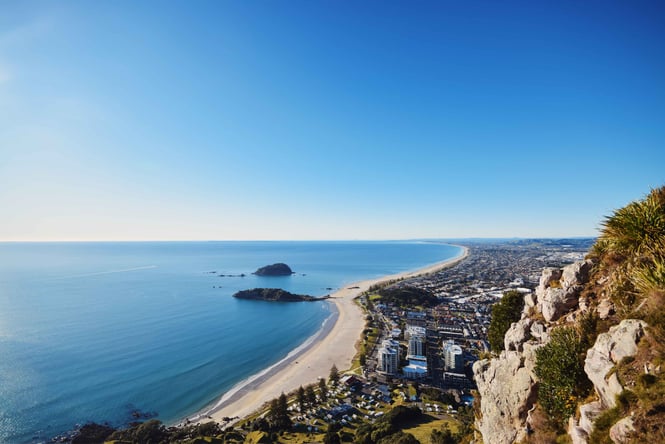 Mount Manganui on a sunny day next to the blue ocean.