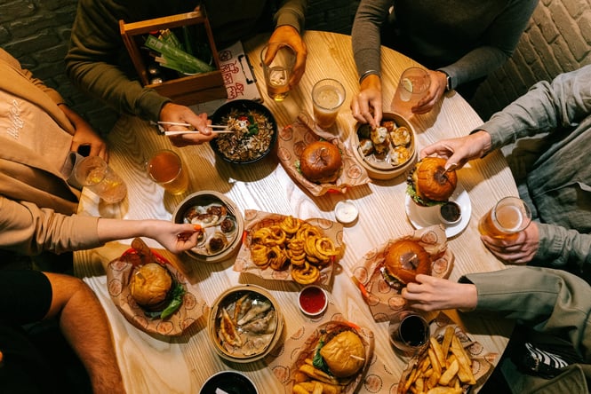 A flatly of burgers and beers on a table at night.