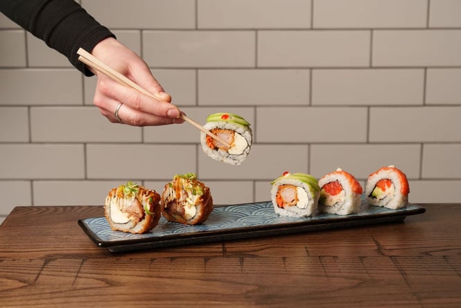 A hand holding chopsticks holding on to a piece of sushi.