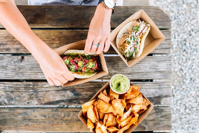Flat lay image of tortilla chips and tacos on a wooden table.