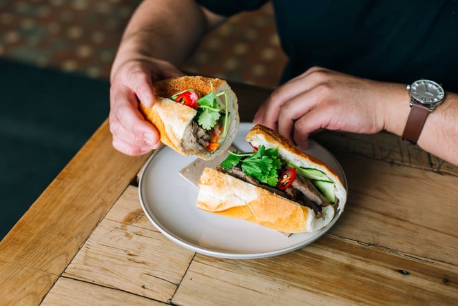 Hands holding a banh mi at a table.
