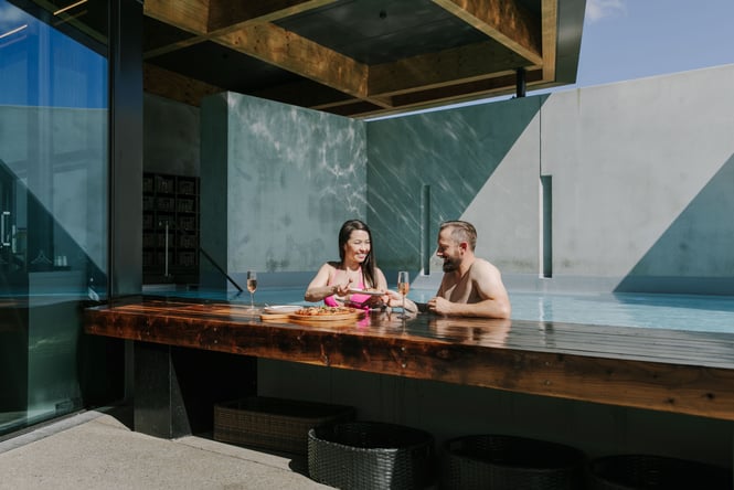A man and woman eating pizza at the pool bar.