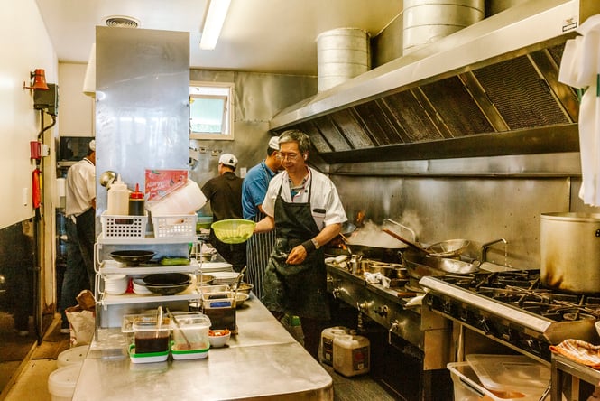 Staff members working inside a busy Chinese restaurant kitchen.