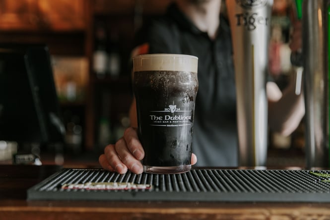 A close up of a hand holding a glass of Guinness.