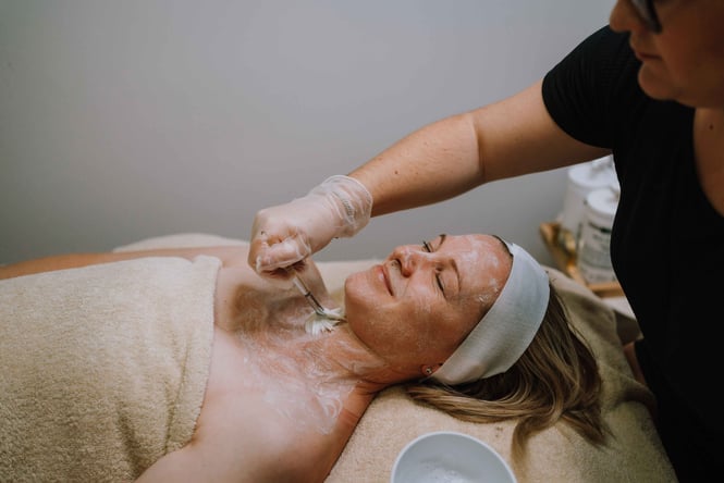A woman with her eyes closed smiling whilst receiving a facial.