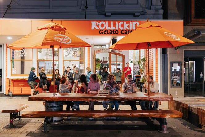 A group of people sitting at a large table outside Rollickin' at night.